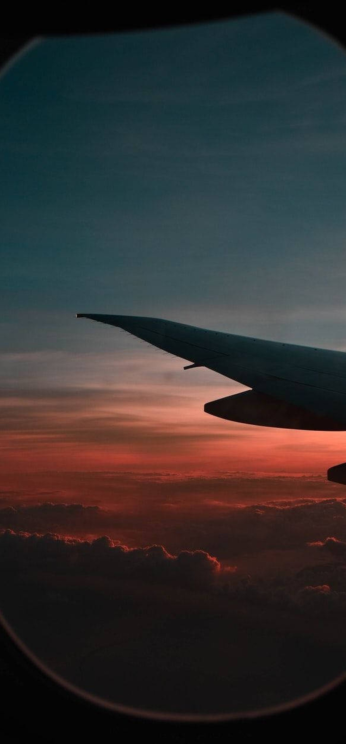Airplane wing silhouetted against a vibrant sunset sky seen through a window.