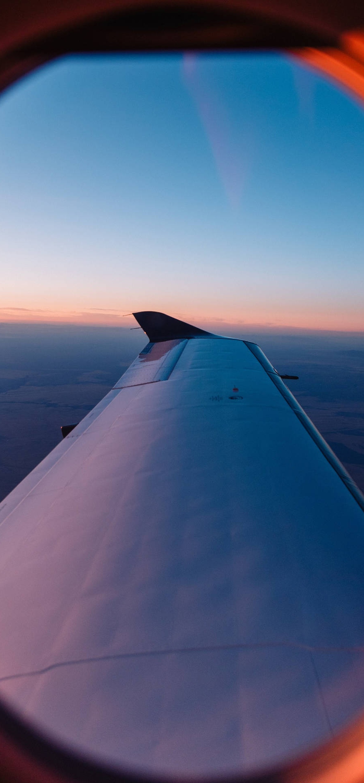 Airplane wing seen from window during sunset with orange glow.