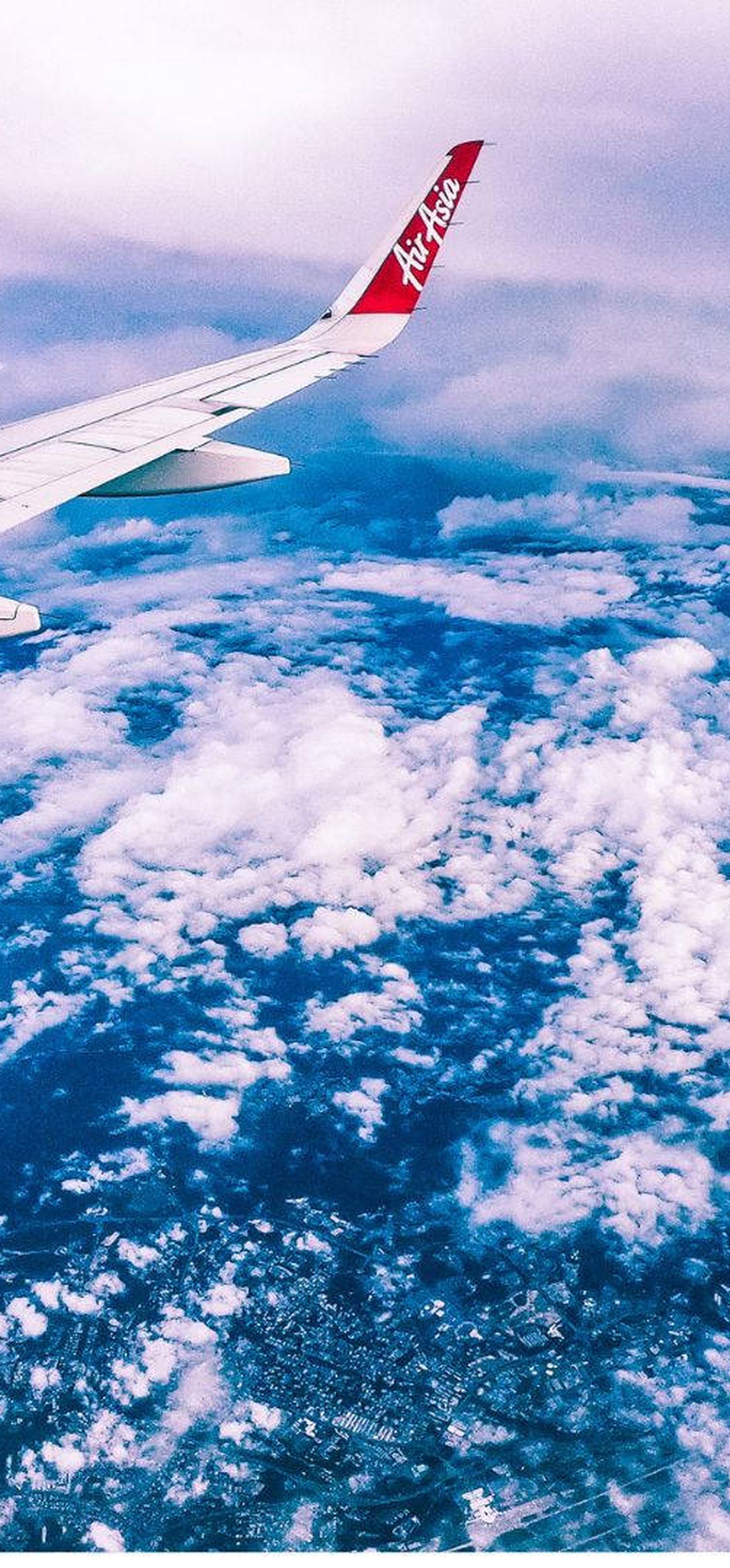 Aircraft wing seen from airplane window above clouds and ocean.