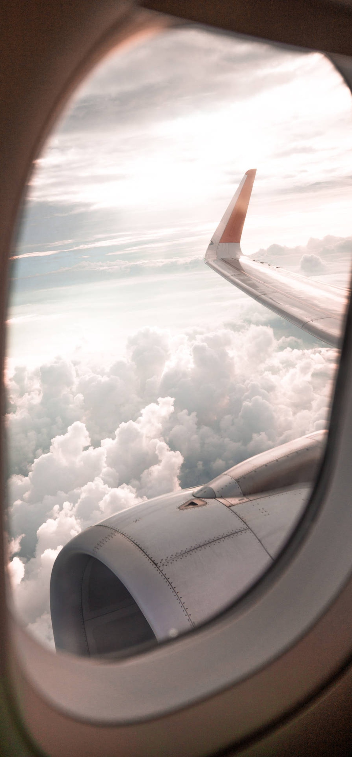 Airplane wing and engine seen through window over clouds at sunrise.