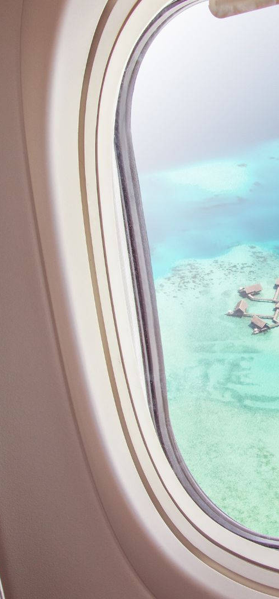 View from airplane window of tropical island with turquoise water and overwater bungalows.