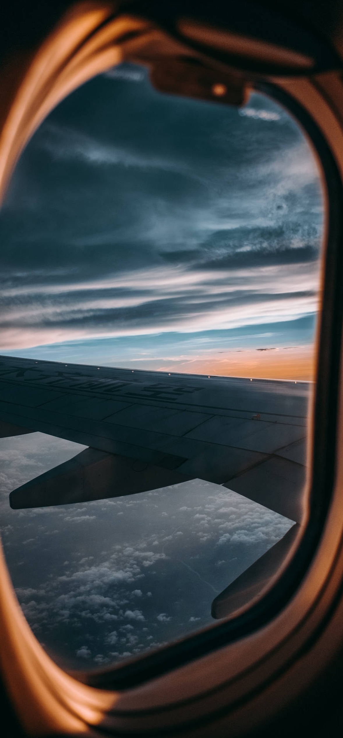 View of airplane wing and clouds through airplane window at dusk.