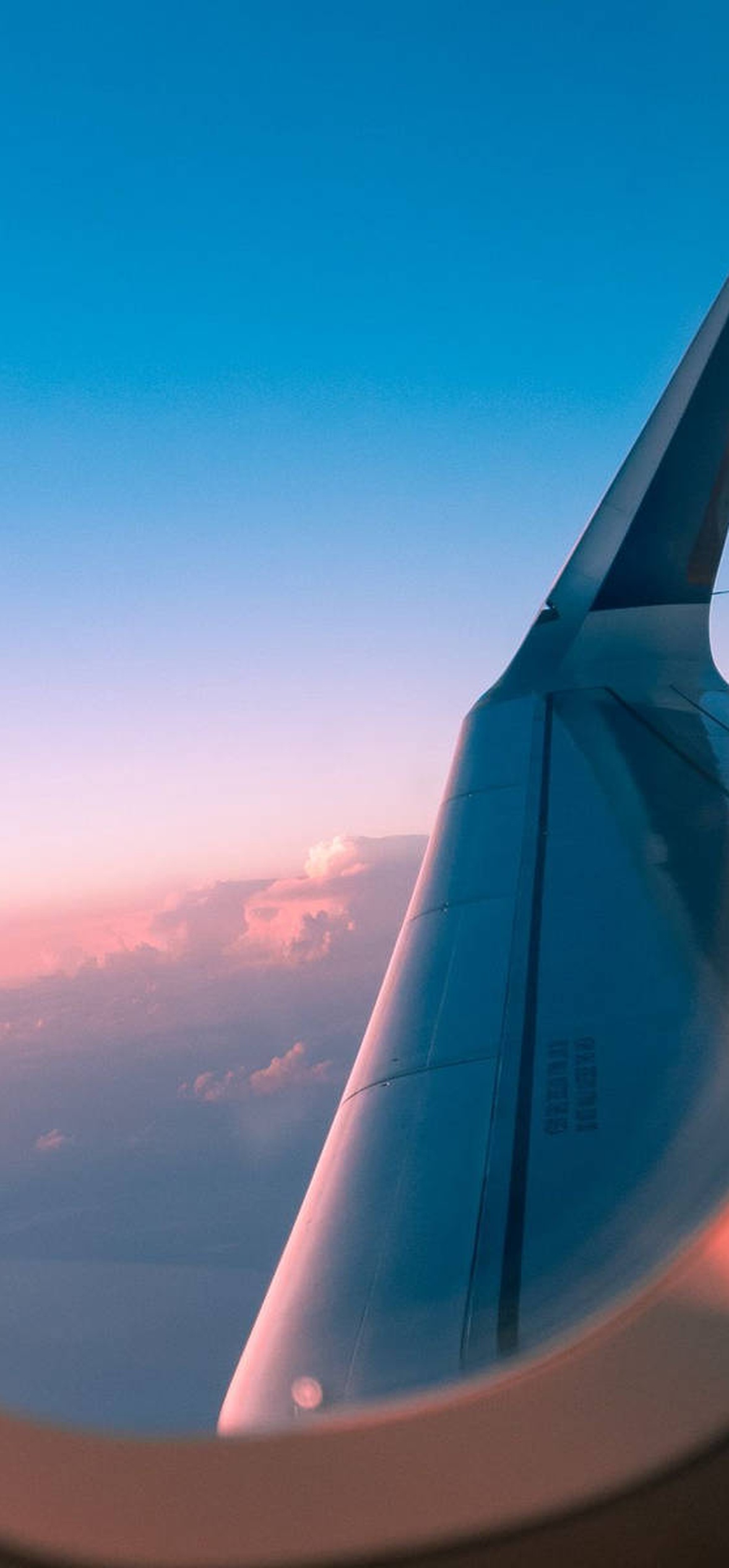 Airplane wing seen from passenger window during sunset with colorful sky.
