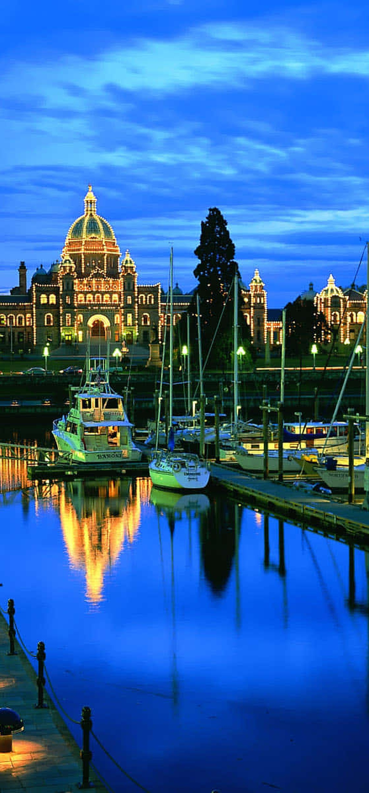 City waterfront with lit historic building and docked boats at dusk.