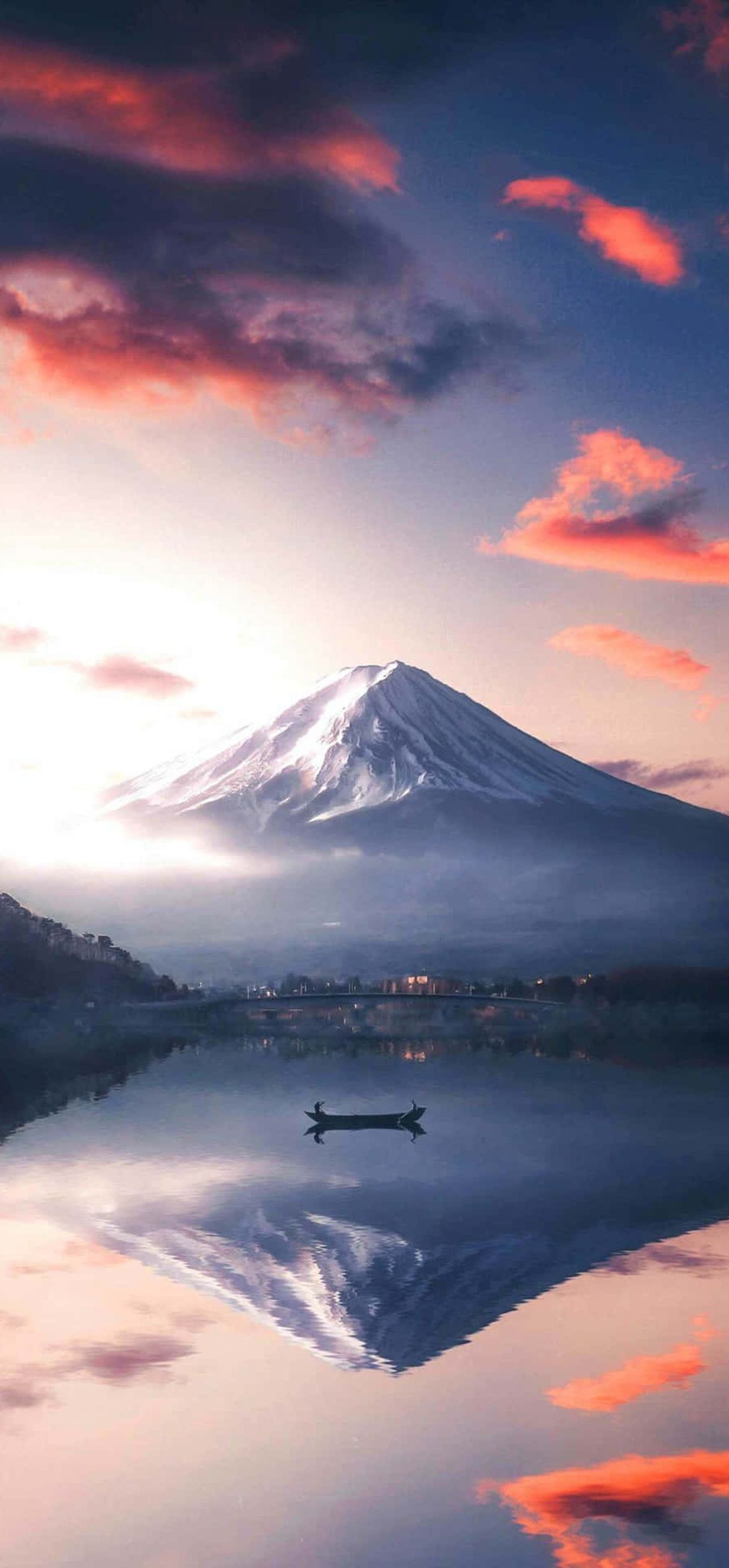 Snowy Mount Fuji mirrored in a tranquil lake with a small boat and colorful sunset clouds.