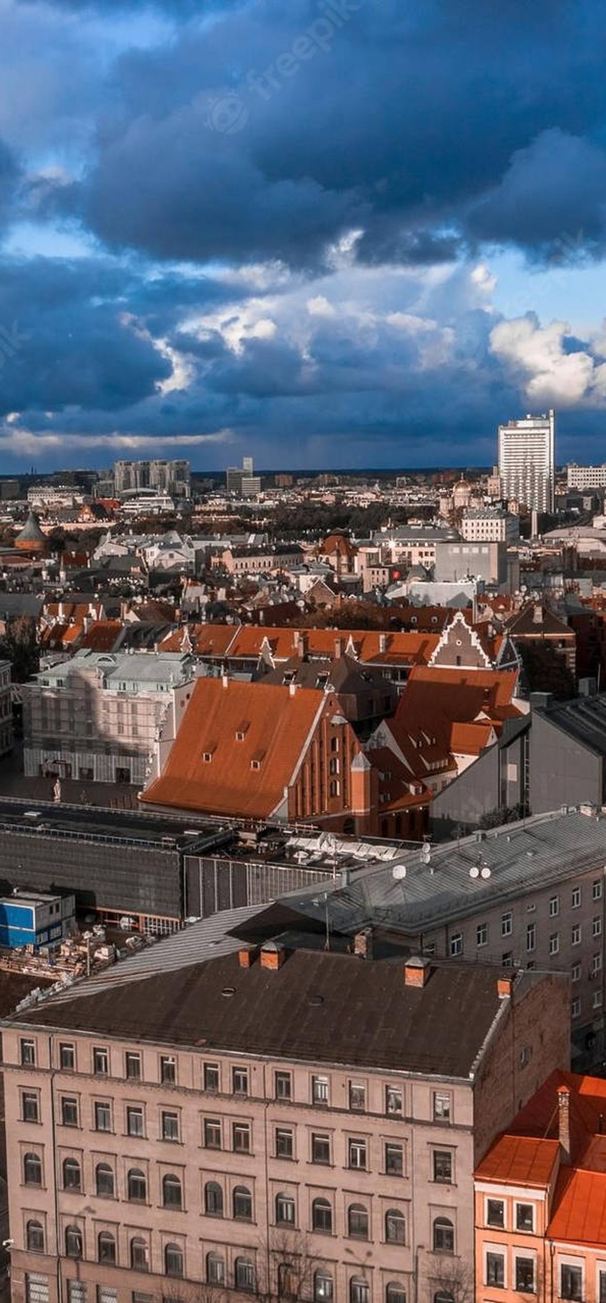 Riga cityscape with red rooftops and a tall spire under stormy clouds.