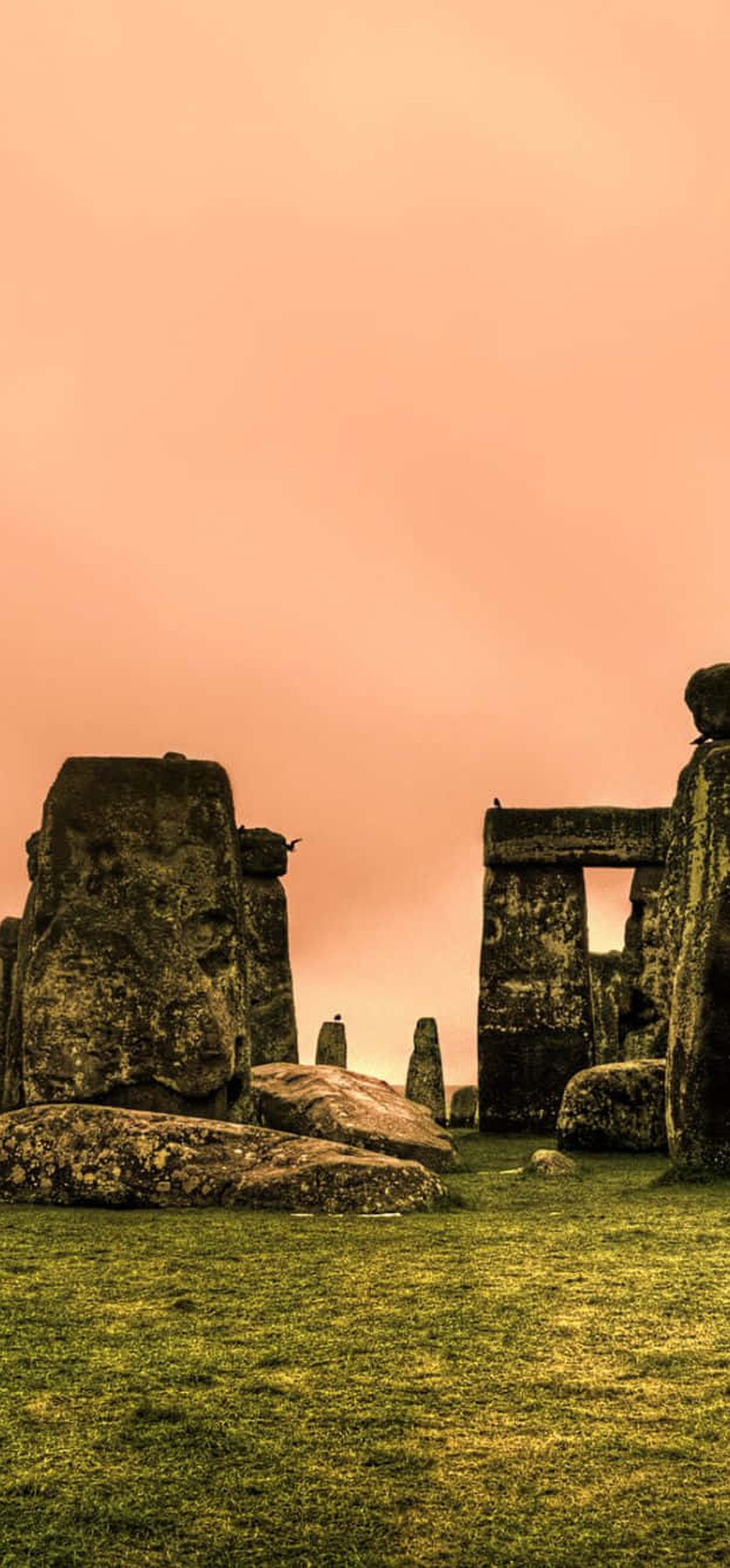 Stonehenge standing stones under a peach sky with green grass foreground