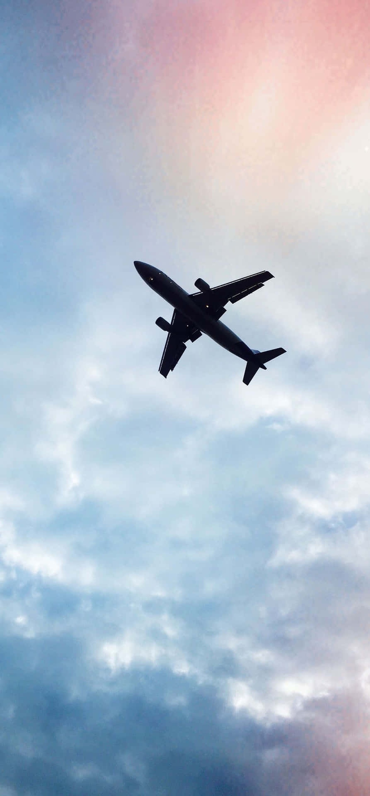 Silhouette of an airplane flying against a colorful sunset sky with scattered clouds.