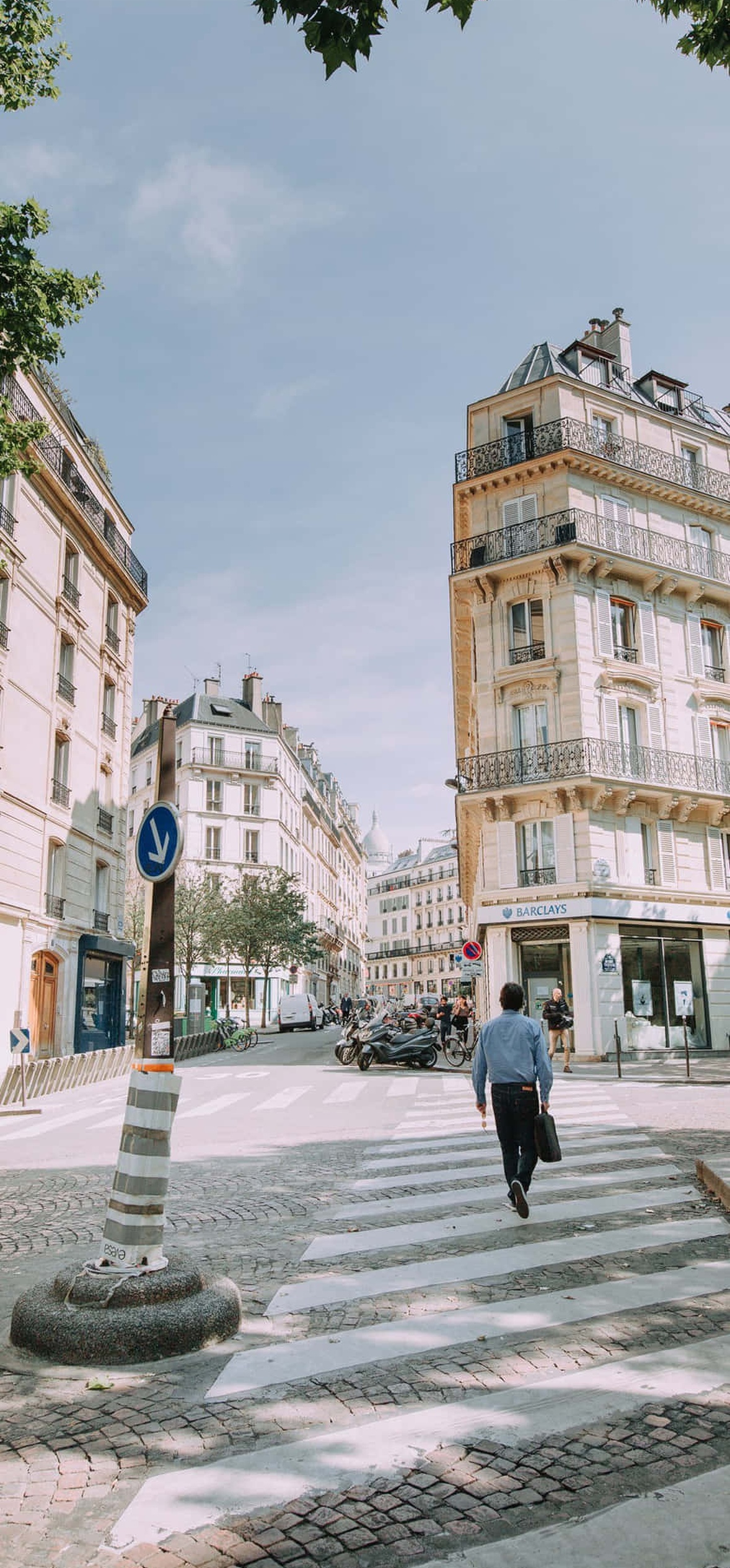 A man crossing a pedestrian street in a European city with historic buildings and trees.