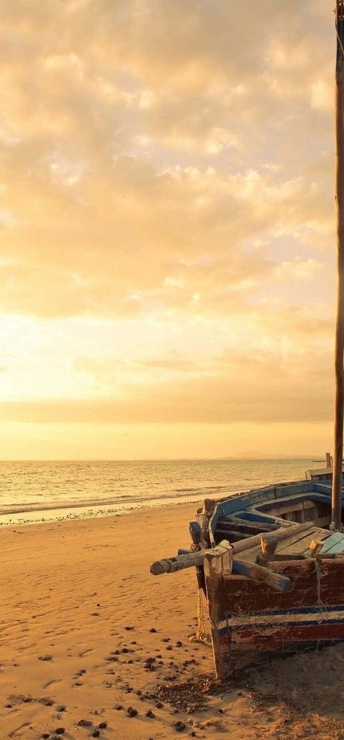 A wooden fishing boat on a sandy beach at golden sunset.