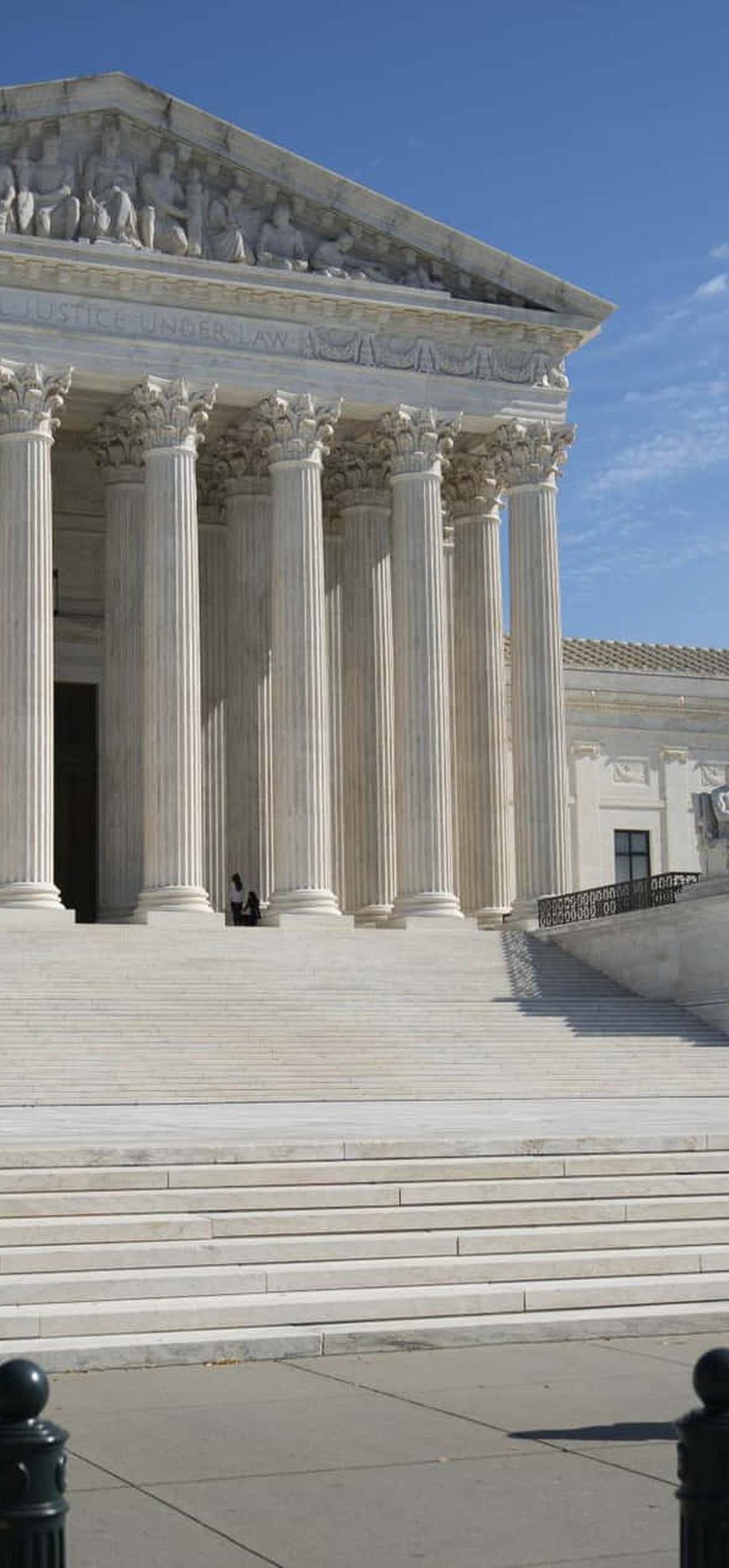Two people walking toward the Supreme Court building on a sunny day.