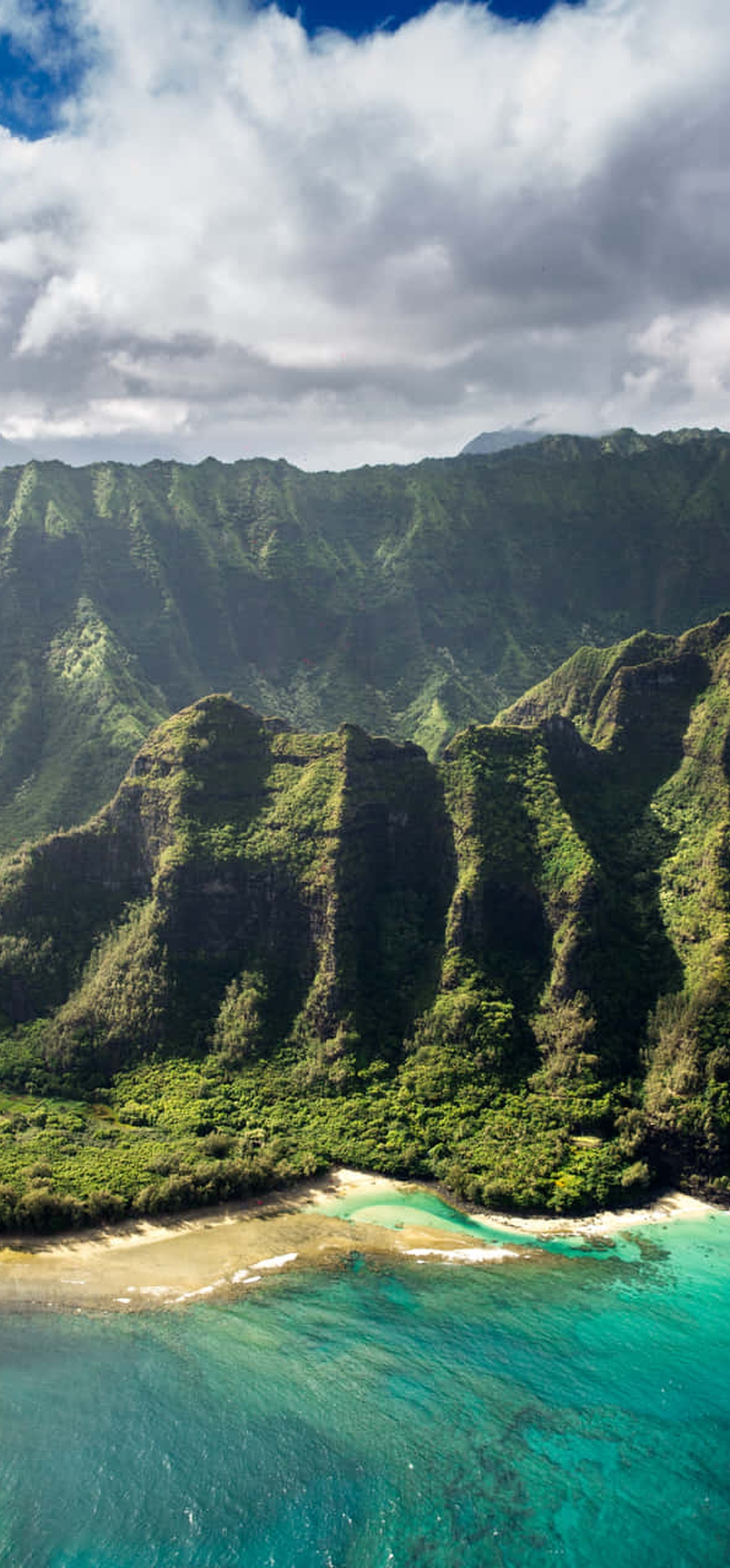 Lush green mountains meet turquoise ocean with white waves crashing on sandy shores.