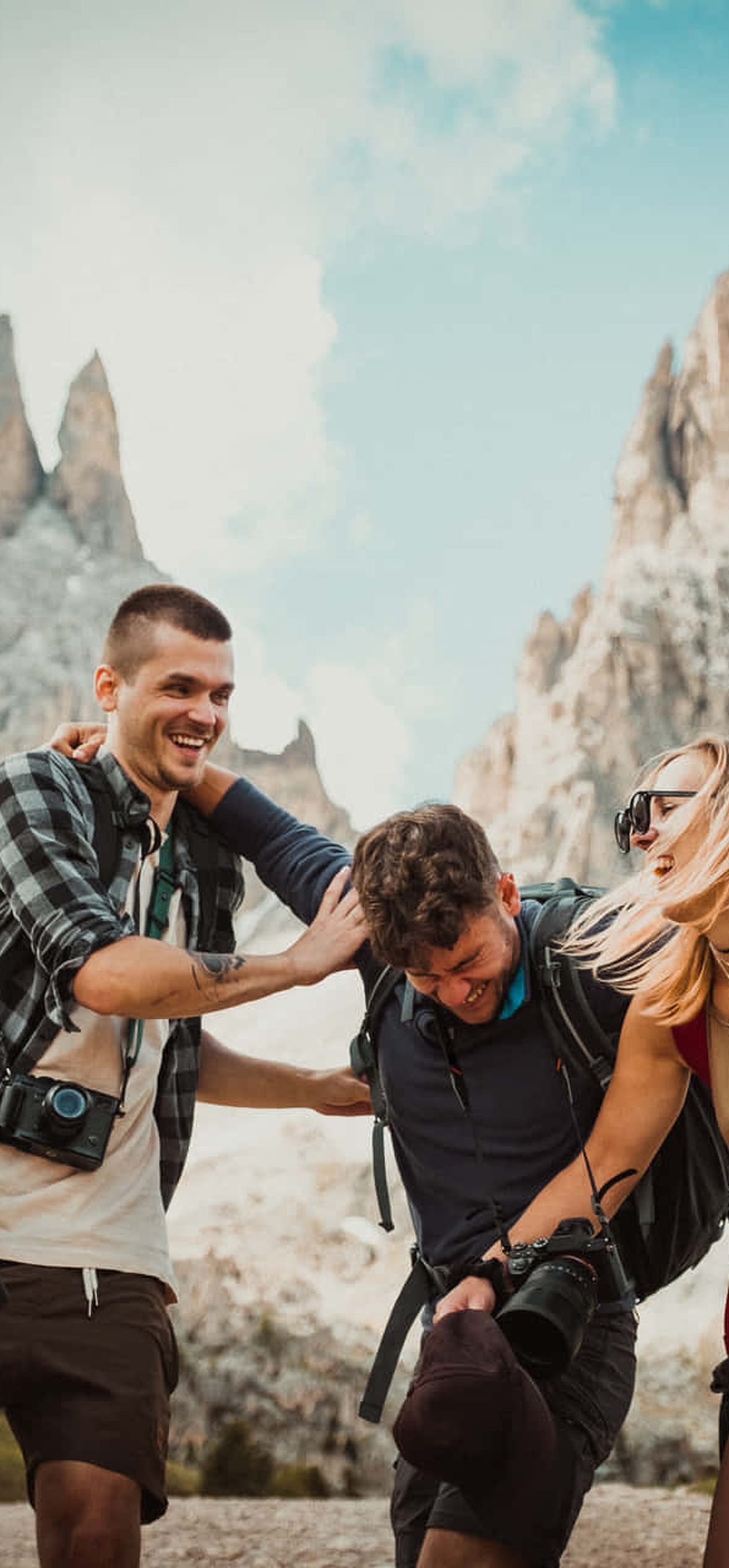 Four friends hiking in mountains with backpacks and cameras laughing together.